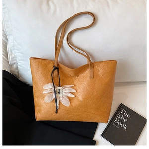 Detail of orange tote bag showing pebbled leather texture and flower charm