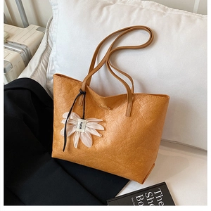 Close-up of mustard yellow leather tote bag with unique texture and flower pendant