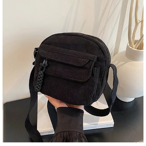 Détail de la texture en velours côtelé noir et poche à rabat sur un sac bandoulière carré