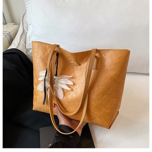 Close-up of a yellow tote bag with wavy leather texture and a white flower charm accessory