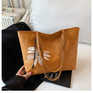 Close-up of bright orange tote bag with white flower charm and wrinkled texture