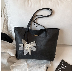 Close-up of black tote bag with wrinkled texture, gold logo, and white flower charm detail