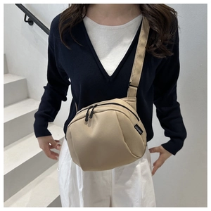 Close-up of beige nylon crossbody shell bag with adjustable strap on a minimalist model