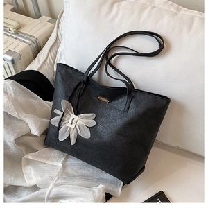 Detail of black embossed tote bag featuring fine cracked texture and a white flower charm