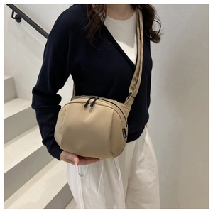 Detail of minimalist beige shell bag with dual zippers and woven label on white stairs