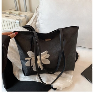 Detail of black pleated PU leather tote bag with white floral applique and FUOR label