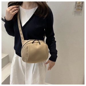 Minimalist beige shell bag shown with crossbody strap on model wearing casual long skirt