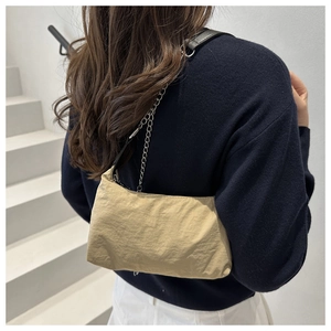 Detail of khaki nylon underarm bag with silver chain strap worn by a model in a minimalist setting