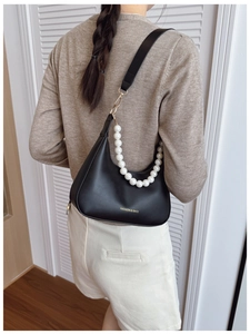 Detail of black crescent shoulder bag featuring gold hardware and a large pearl chain strap