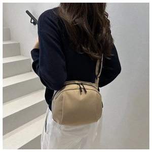 Adjustable beige crossbody bag with curved design shown on model in urban casual setting
