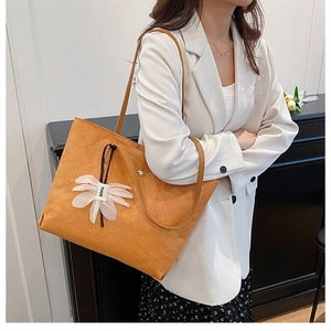 Detail of orange tote bag with a floral charm on a white blazer outfit for daily commute
