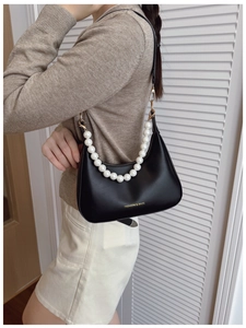 Close-up of black leather underarm bag featuring decorative large white pearl chain handle