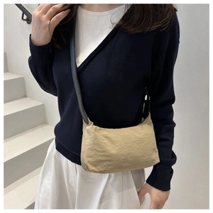 Detail of khaki pleated nylon crossbody bag shown on model in a minimalist setting