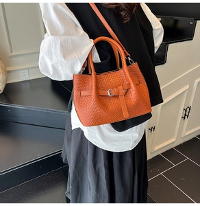 Detail of woven orange handbag featuring a leather buckle and crossbody strap design