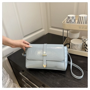 Détail du sac à main en cuir verni bleu clair avec boucle cœur dorée et longue lanière