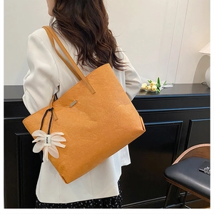 Ingwergelbe Shopper-Tasche mit Faltenstruktur und weißem Blumenanhänger am Damenmodell