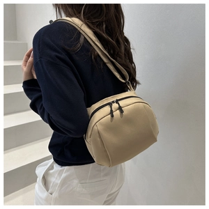 Gros plan d'un sac bandoulière kaki minimaliste porté par un mannequin sur un escalier blanc