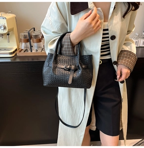 Détail du sac à main noir tressé avec boucle décorative et double poignées arrondies