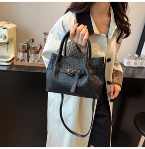 Dettaglio di borsa tote intrecciata nera con fibbia in metallo su bancone caffè