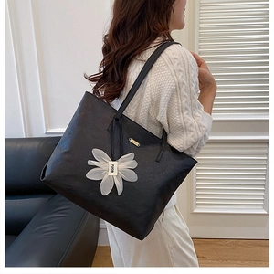 Side view of large black tote bag with white flower charm worn by a model in lifestyle setting