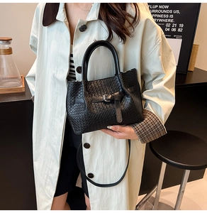 Détail du sac à main noir en cuir tressé avec boucle argentée et poignées dans un café