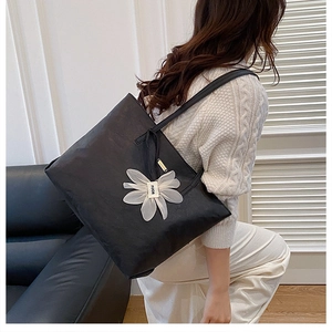 Detail of a large black leather tote bag with a white floral charm on a female model