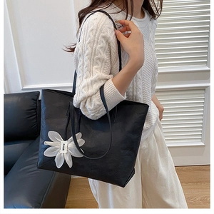 Detail of a black textured tote bag featuring a white flower charm and ruffled accents