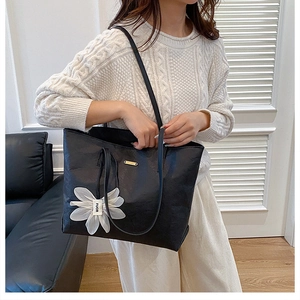 Detail of a large black tote bag with white flower charm and fine leather texture