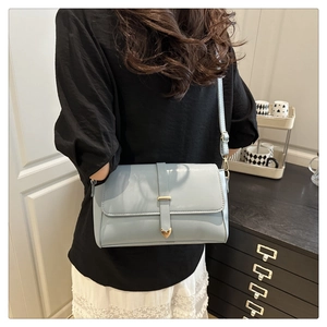 Détail du sac bandoulière bleu clair avec boucle en forme de cœur doré et bandoulière
