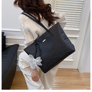 Detailed back view of a black tote bag with white floral charm on a model