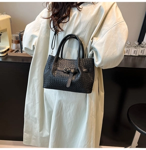 Dettaglio della borsa nera intrecciata con fibbia decorativa e manici in pelle liscia