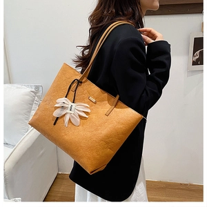 Detail of vintage brown tote bag featuring pleated leather texture and white floral charm