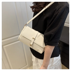 Gros plan d'un sac à bandoulière blanc minimaliste avec un pendentif coeur doré et rabat