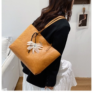 Detail of vintage crinkled leather tote bag in yellow with a floral charm