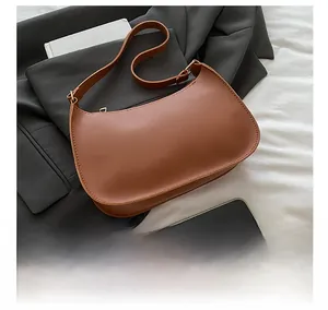 Brown moon-shaped shoulder bag size comparison with smartphone on grey blazer