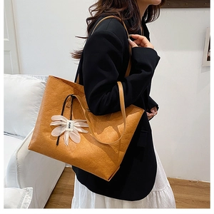 Detail of vintage camel tote bag with flower charm and textured leather on model