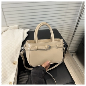 Détail du petit sac carré beige avec boucle argentée posé sur un siège en cuir