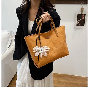 Close-up of caramel tote bag with faux leather texture and white daisy charm detail