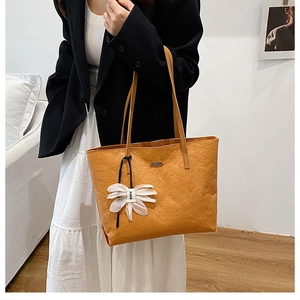 Detail of orange-brown textured tote bag with flower charm worn on shoulder