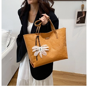 Detail of caramel tote bag with pleated texture and white flower charm pendant