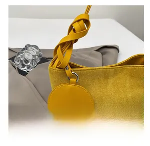 Dettaglio della borsa a secchiello giallo zenzero opaco con manico a treccia e ciondolo