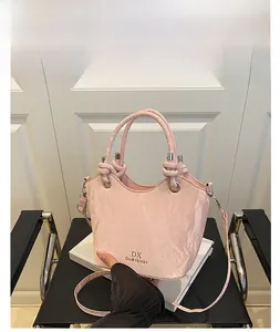 Détail du sac seau rose avec texture plissée et logo doré sur le devant