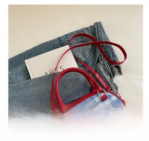 Detail view of plaid handbag with red leather handles and strap on denim jeans