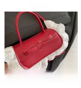 Close-up of red leather handbag featuring a leather bow and white scalloped lace trim