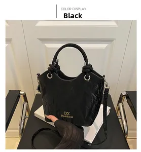 Gros plan du sac seau noir avec texture plissée et logo doré posé sur un livre blanc