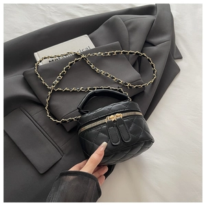 Detailed view of black quilted mini box bag with gold double zippers and chain strap