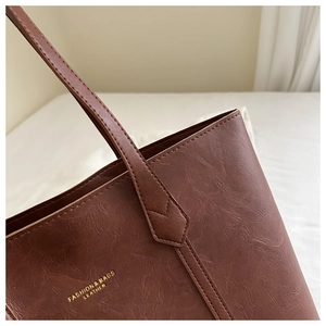 Détail macro du sac cabas marron foncé avec logo doré et texture de cuir fine