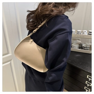 Side view of a minimalist beige crescent shoulder bag worn with a dark blue top