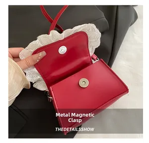 Close-up of silver magnetic clasp on red leather handbag with white lace trim detail