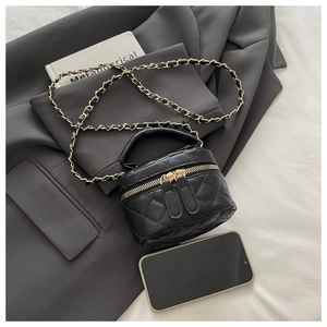 Detail of a black quilted mini vanity bag with gold zippers and chain strap on grey fabric